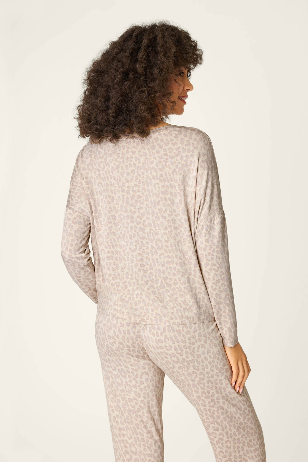 A person with curly hair is seen from the back wearing the P.J. Salvage Luxe Leopard Dreams Long Sleeve Top and matching pants in a light beige animal print, set against a plain, light background.