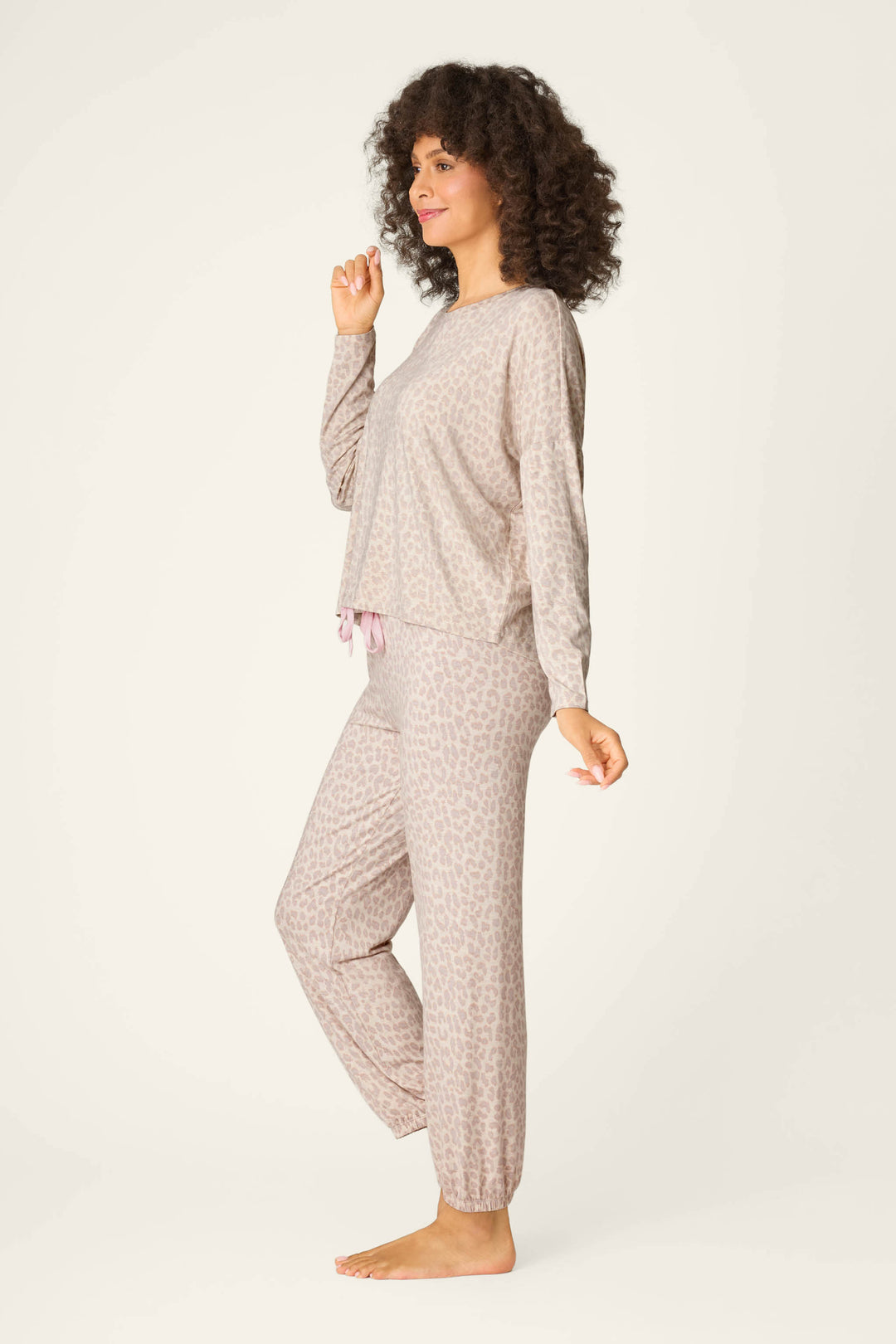 A person stands barefoot against a plain background, wearing the Luxe Leopard Dreams Lounge Set by P.J. Salvage—a relaxed, long-sleeve top and jogger pants set that's breathable and perfect for comfortable lounging.