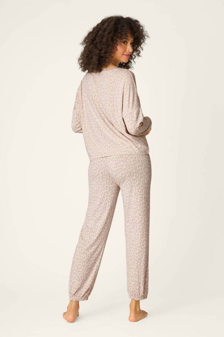 A woman with curly hair stands barefoot, facing away, in the P.J. Salvage Luxe Leopard Dreams Lounge Set—a matching long-sleeve pajama set with a subtle leopard print on soft jersey, perfect for all-night comfort.