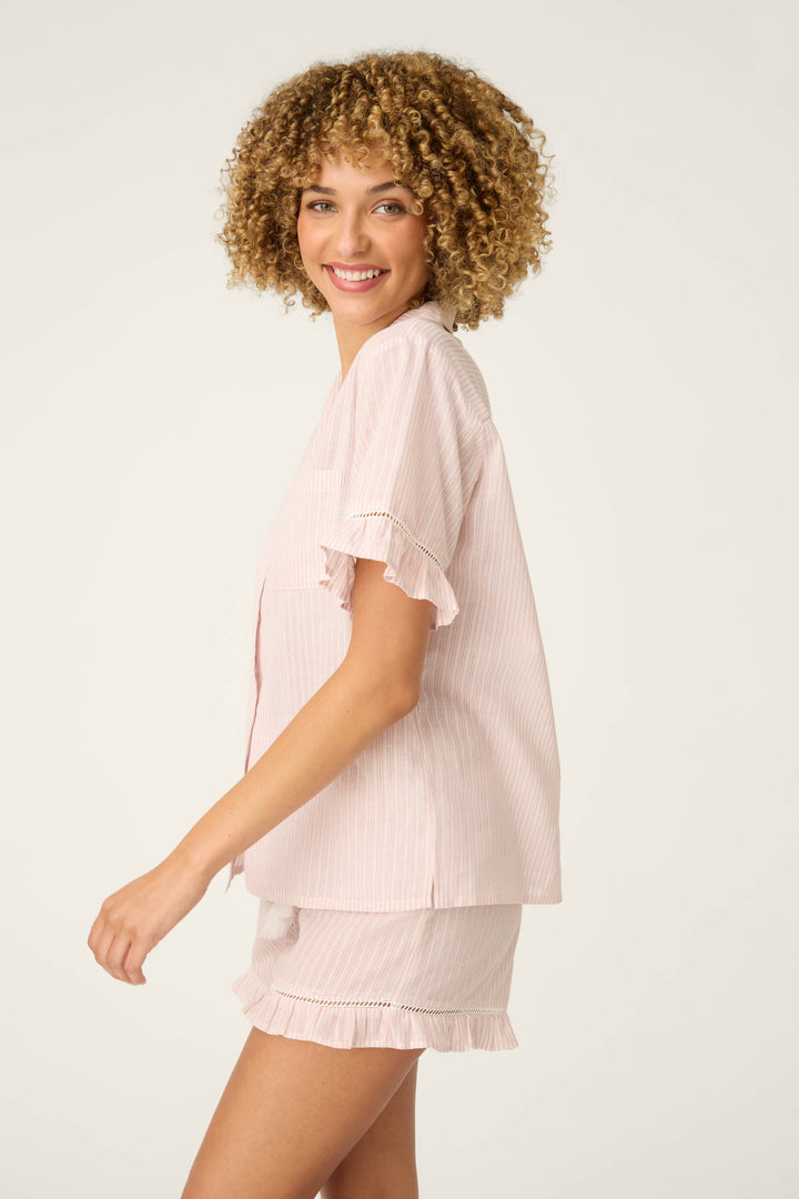 A person with curly hair is smiling and wearing the P.J. Salvage On Cloud Nine Silver Rose Short Sleeve Pajama Top, standing against a plain light background.