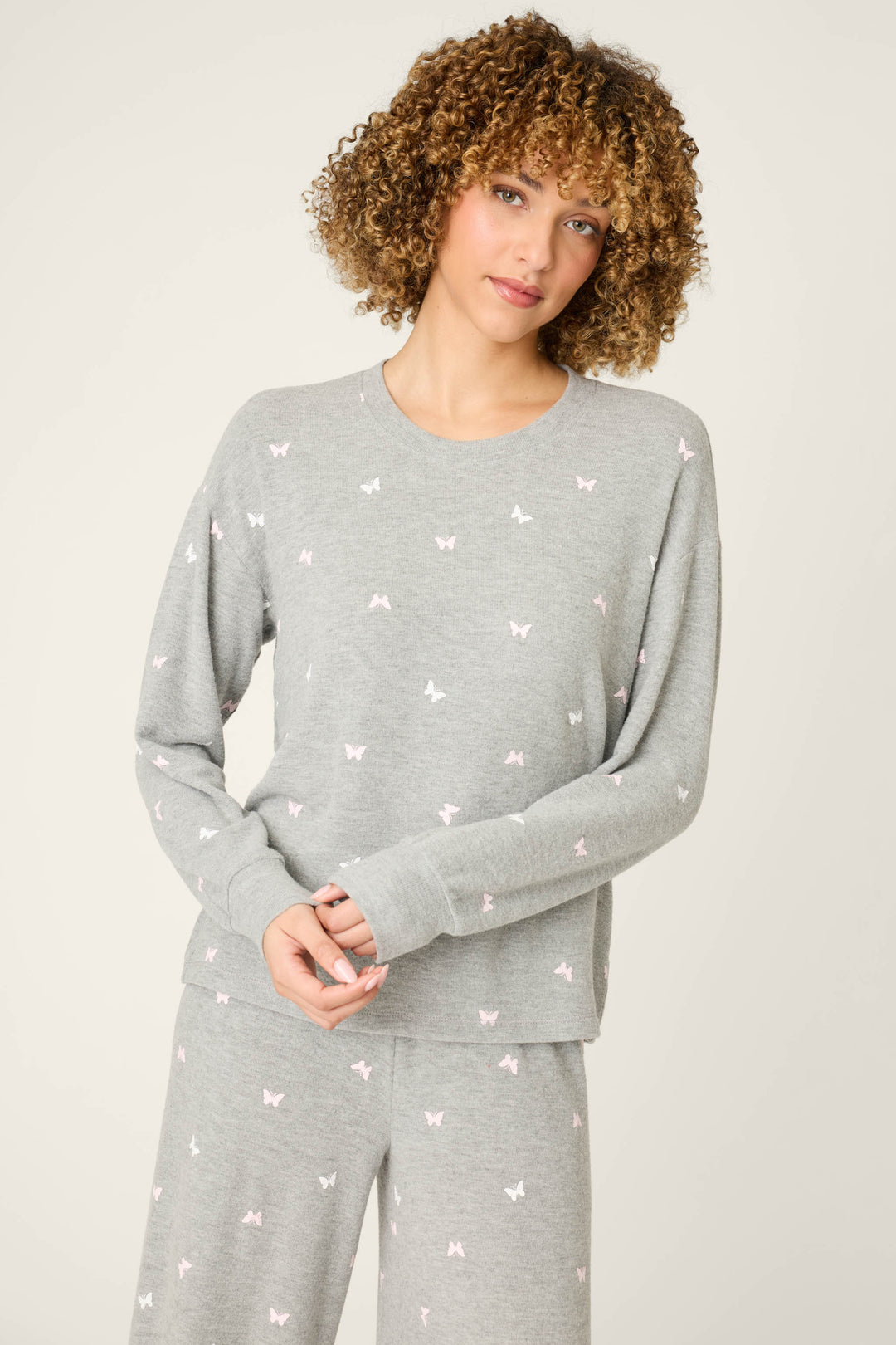 A person with curly hair wears the P.J. Salvage Peachy Mix & Match Butterfly Kisses Long Sleeve Top in heather grey, standing against a plain off-white background.