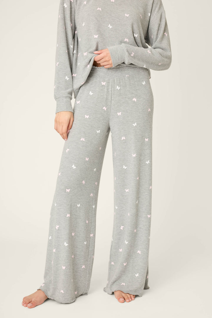 A person wears P.J. Salvage Peachy Mix & Match Butterfly Kisses Open Leg Lounge Pants, featuring a grey wide-leg design and small white and pink butterfly print. Their feet are bare, and their face is not shown in the image.