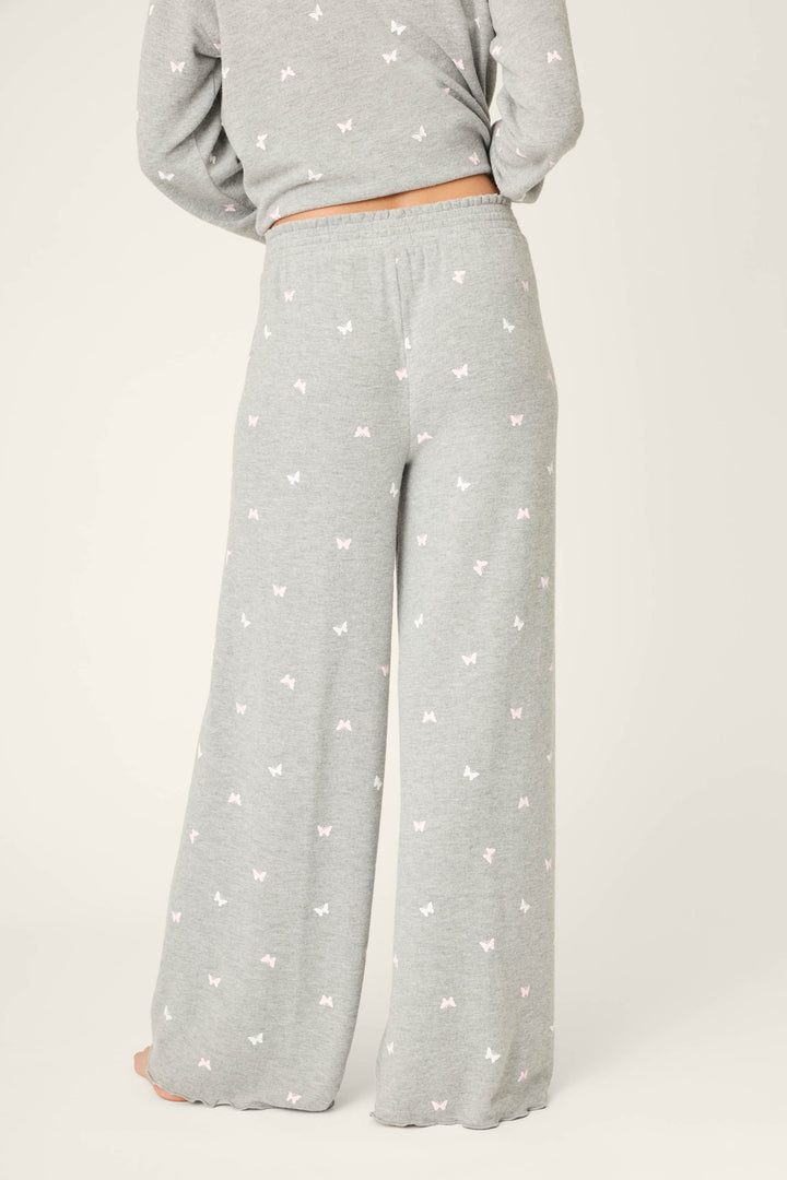 A person is seen from the back wearing P.J. Salvage Peachy Mix & Match Butterfly Kisses Open Leg Lounge Pants in light gray, featuring a white and pink butterfly print, elastic waistband, and paired with a matching top for a cozy look.