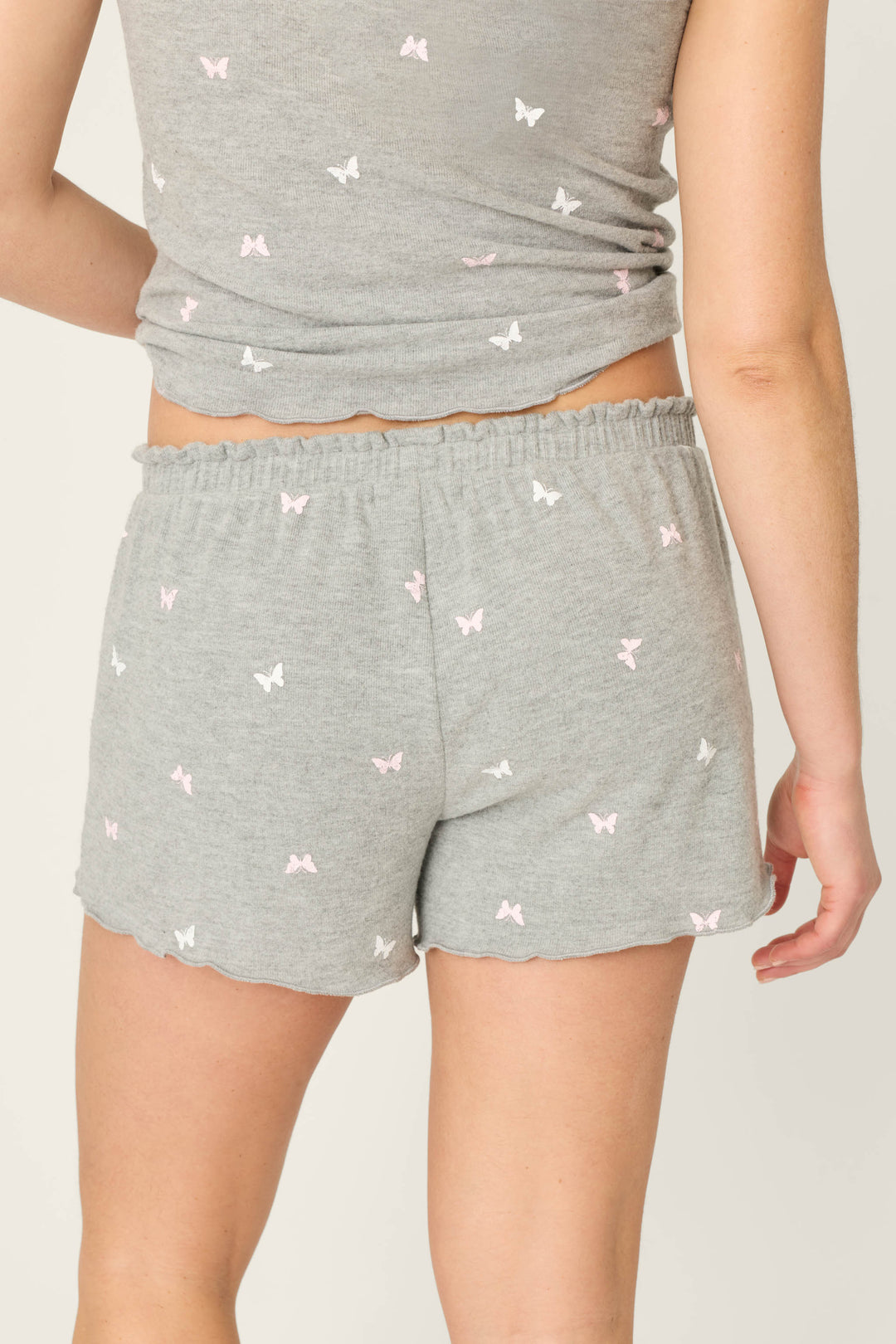 A person is shown from the back wearing P.J. Salvage Peachy Mix & Match Butterfly Kisses Shorts in heather grey, paired with a matching tank top featuring a small white butterfly print, highlighting the shorts and part of the top.