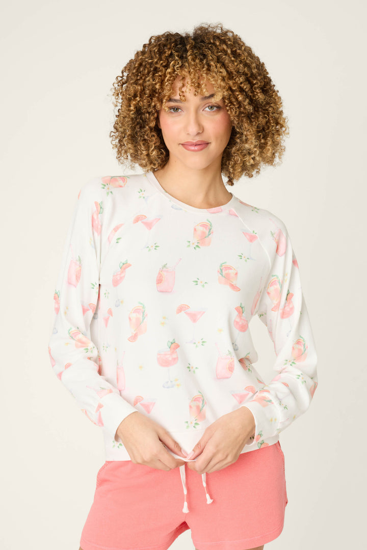 A person with curly hair wears the P.J. Salvage Paloma Mama Sweet Sips Long Sleeve Top and pink drawstring shorts, standing against a plain light background.