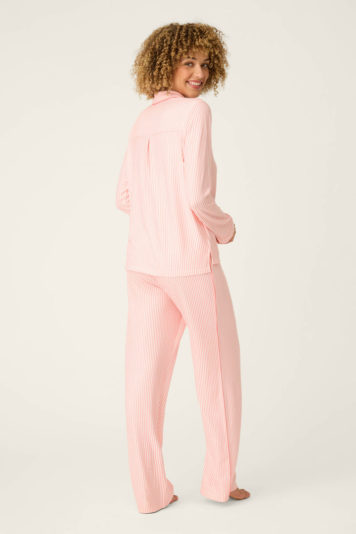 A person with curly hair stands barefoot, looking back over their shoulder, modeling the Paloma Mama Sweet Stripes Long 3-Piece PJ Set by P.J. Salvage in grapefruit pink with white stripes against a plain light background.