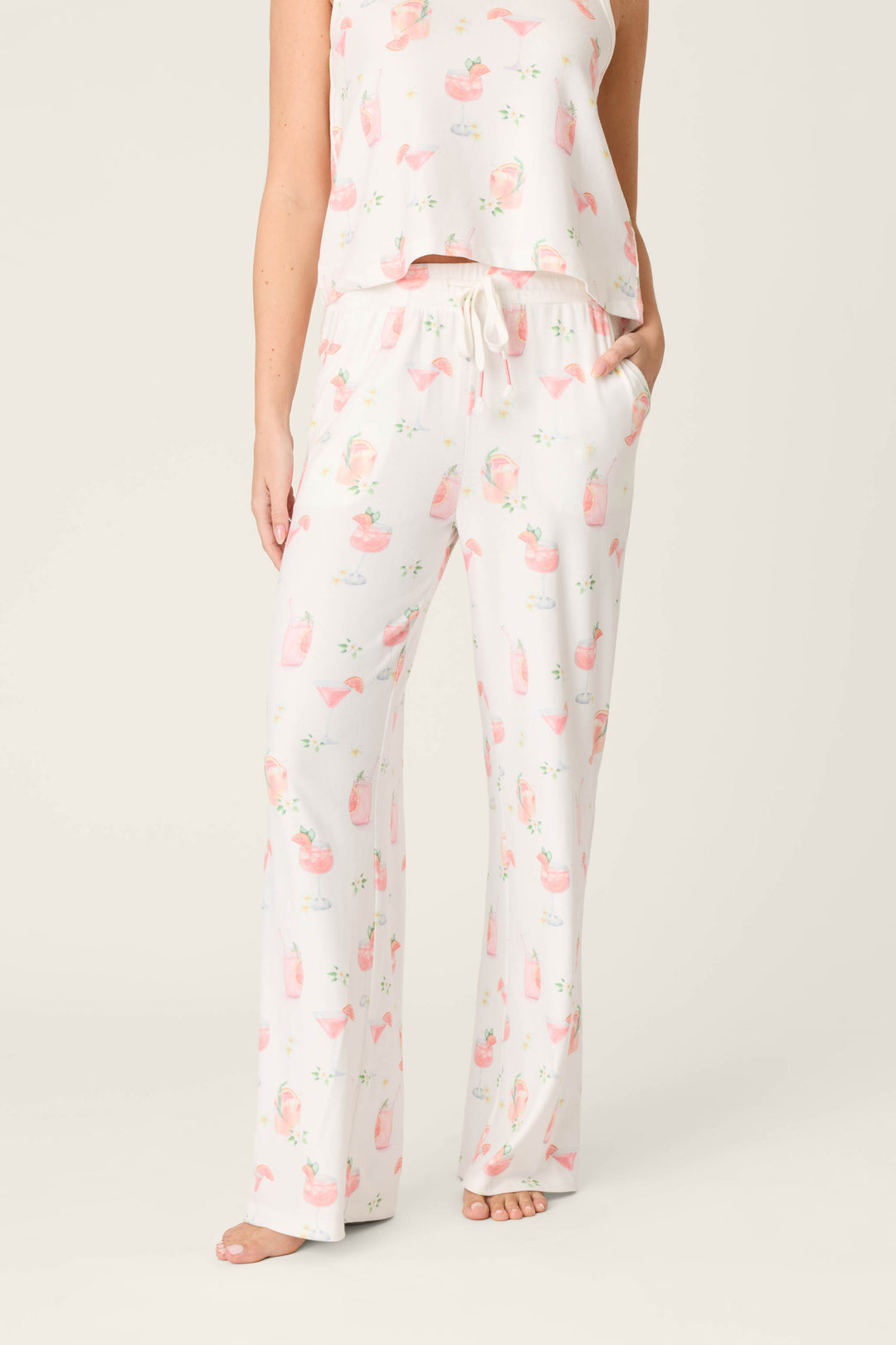 A person wears P.J. Salvage Paloma Mama Sweet Sips Open Leg Pajama Pants in ivory with a cocktail print, paired with a matching top, standing barefoot against a plain light background; their head and upper torso are not shown.