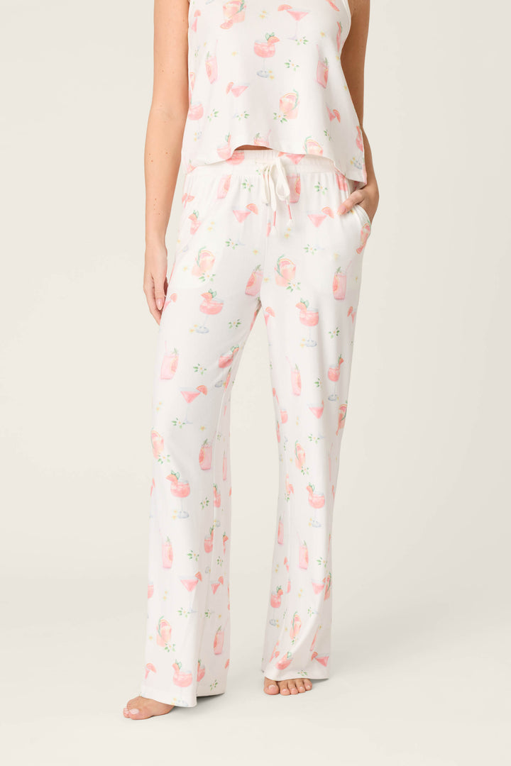 A person wears P.J. Salvage Paloma Mama Sweet Sips Open Leg Pajama Pants in ivory with a cocktail print, paired with a matching top, standing barefoot against a plain light background; their head and upper torso are not shown.