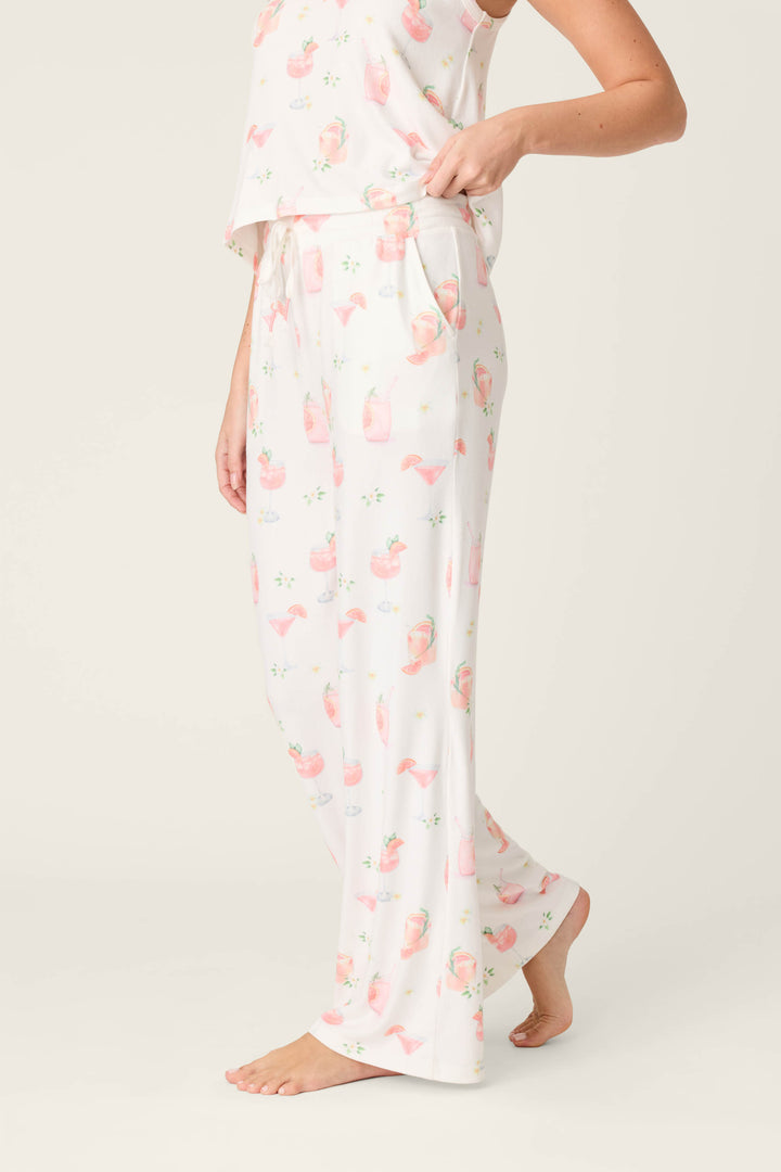 A person models the P.J. Salvage Paloma Mama Sweet Sips Open Leg Pajama Pants in ivory with a playful cocktail print, standing barefoot against a plain light background with one hand in their pocket and their butter jersey pajama top partially visible.