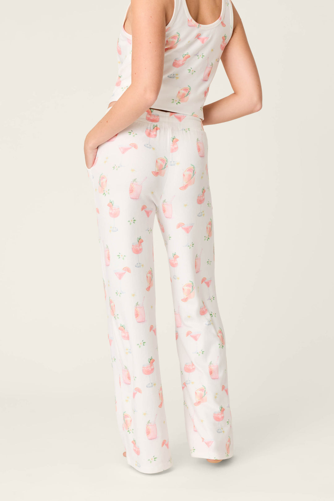 A person models P.J. Salvage's Paloma Mama Sweet Sips Open Leg Pajama Pants—ivory with a playful Paloma cocktail print—standing with one hand in the pocket, facing away from the camera.