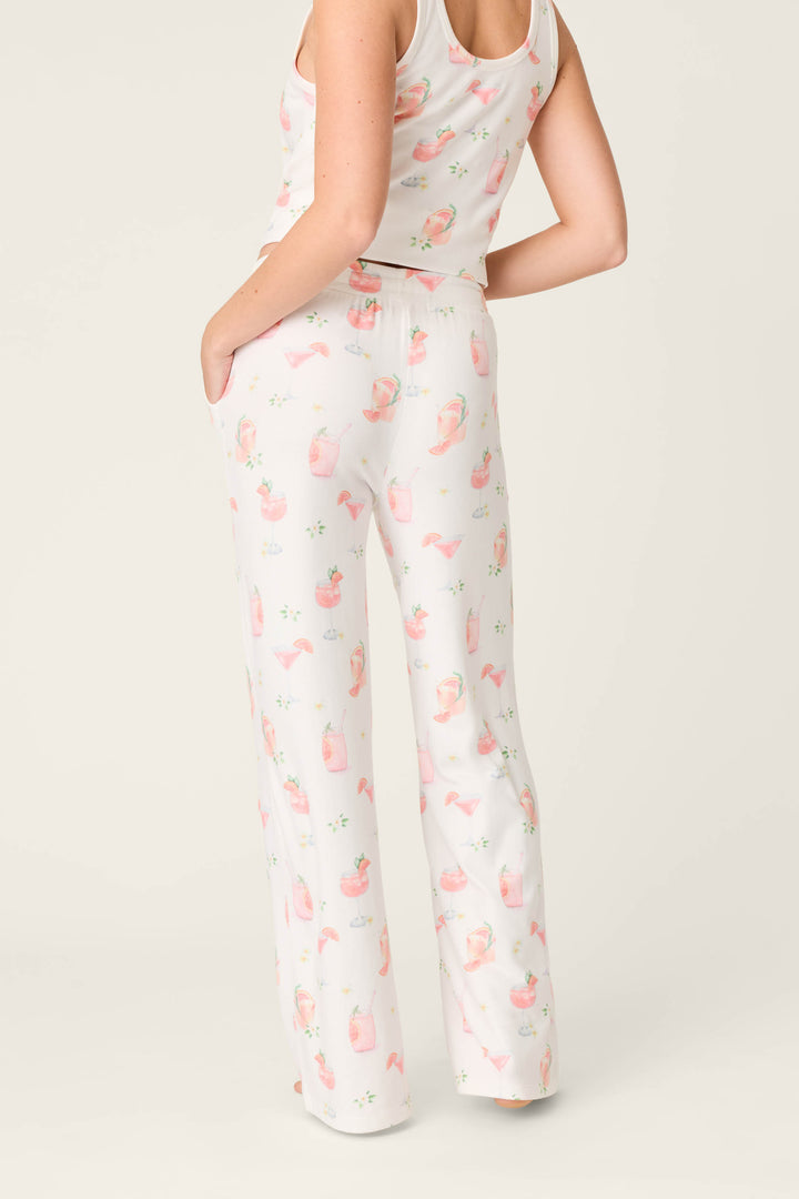 A person models P.J. Salvage's Paloma Mama Sweet Sips Open Leg Pajama Pants—ivory with a playful Paloma cocktail print—standing with one hand in the pocket, facing away from the camera.