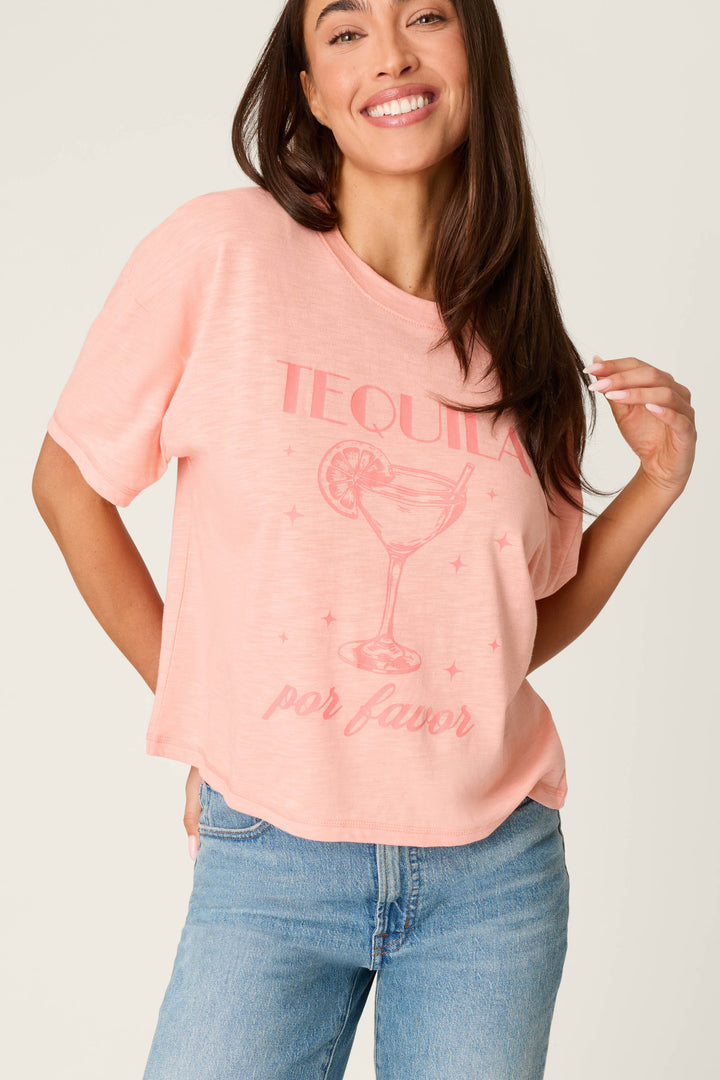 A woman in the P.J. Salvage Paloma Mama Tequila Por Favor Graphic T-Shirt, a grapefruit pink crew tee in soft cotton-modal slub jersey, smiles at the camera. She pairs it with light blue jeans for a comfortable look.
