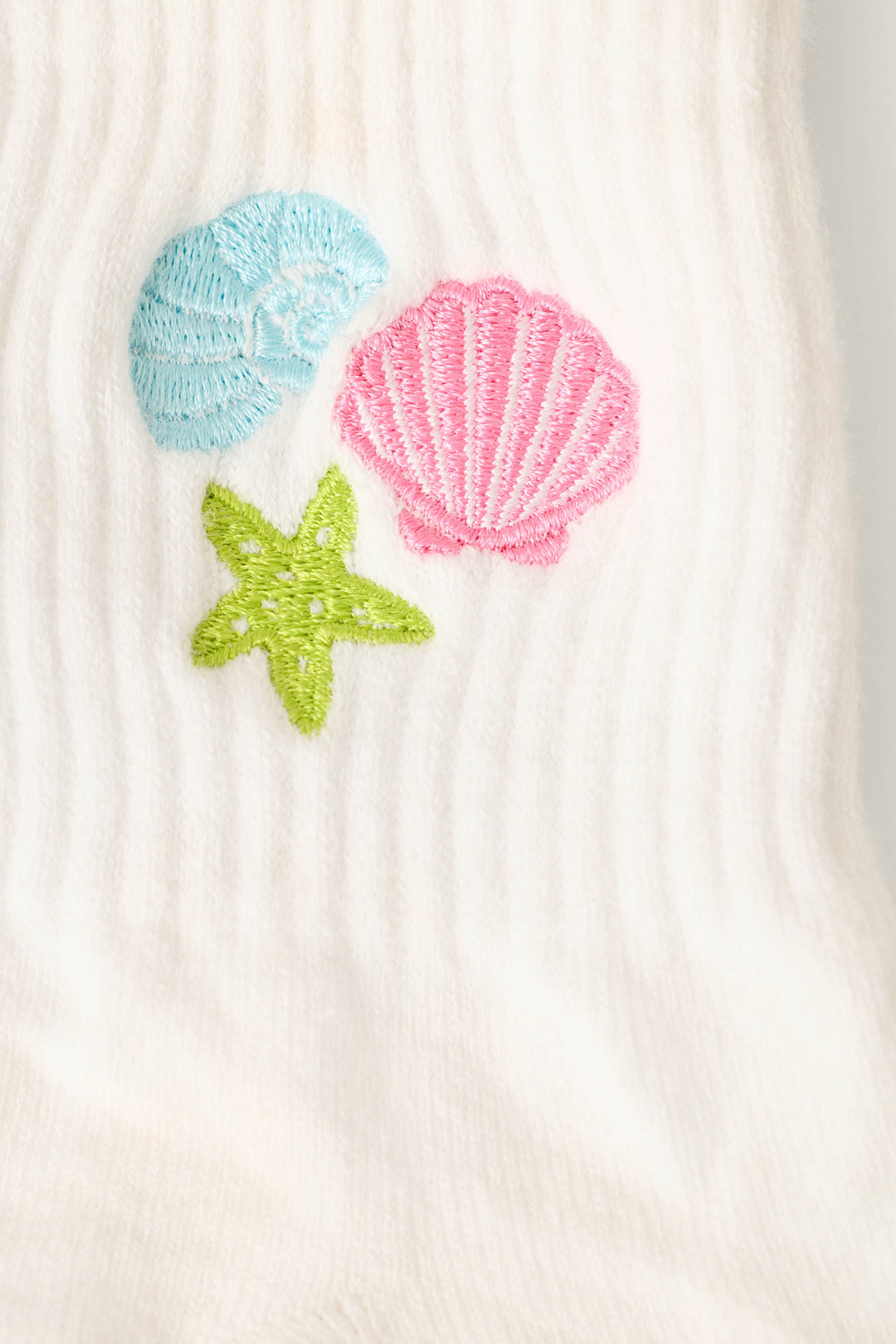 Close-up of P.J. Salvage Playful Prints She Sells Seashells Quarter Crew Socks, showcasing white ribbed fabric with embroidered blue seashell, pink scallop shell, and green starfish designs.