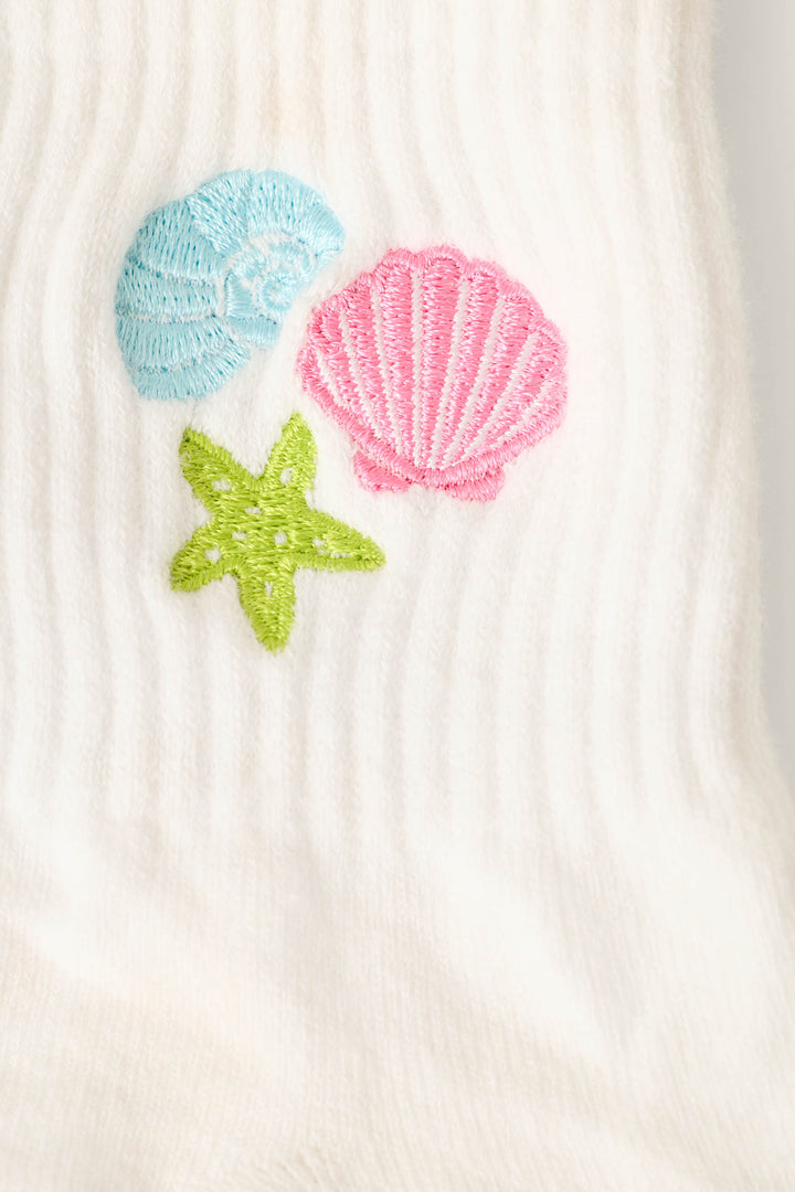 Close-up of P.J. Salvage Playful Prints She Sells Seashells Quarter Crew Socks, showcasing white ribbed fabric with embroidered blue seashell, pink scallop shell, and green starfish designs.