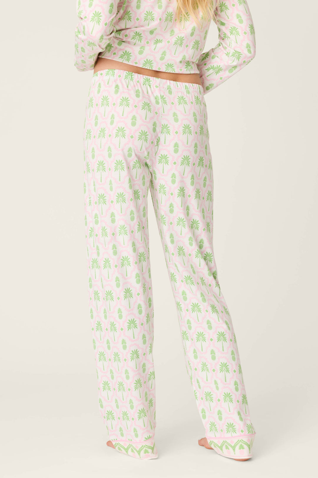 A person faces away, wearing P.J. Salvage Playful Prints Island Time Open Leg PJ Pants with a matching long-sleeved palm tree top. The relaxed ivory set pairs effortlessly with their blonde hair for an easy, breezy vibe.