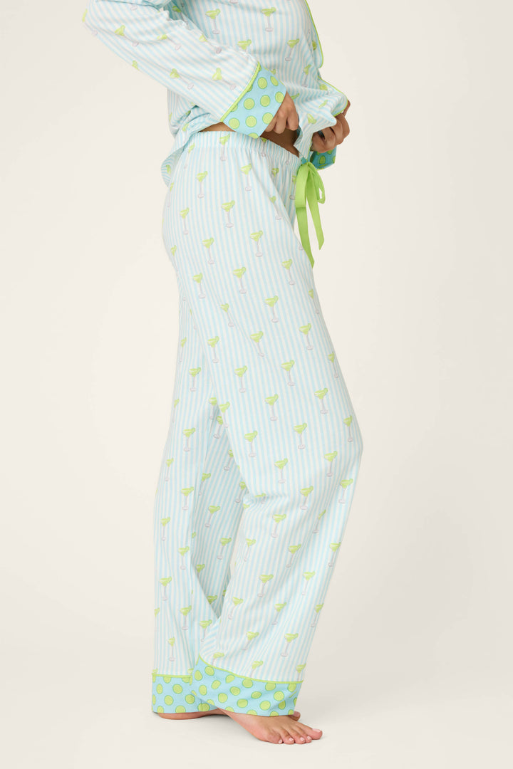 A person is wearing P.J. Salvage’s Playful Prints Island Time Short PJ Set pajama pants in light blue and white stripes, with a green drawstring, green polka dot cuffs, and small green objects. They’re barefoot, upper body partially out of frame.