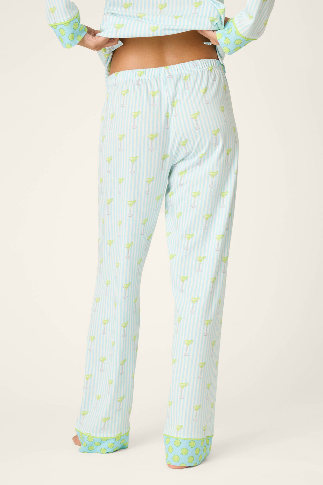 Shown from the back, a person wears P.J. Salvage’s Playful Prints Island Time Short PJ Set—light blue and white vertical stripes with light green accents and wide polka dot cuffs in cotton-modal jersey, plus a matching slightly cropped top.
