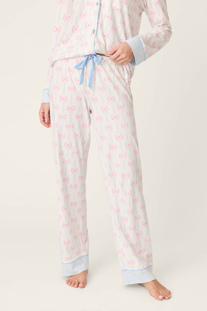 Wearing P.J. Salvage's Playful Prints All Wrapped Up Open Leg PJ Pants with bow print, blue gingham cuffs, and a drawstring waist, a person stands barefoot against a light background, showcasing the open-leg silhouette.