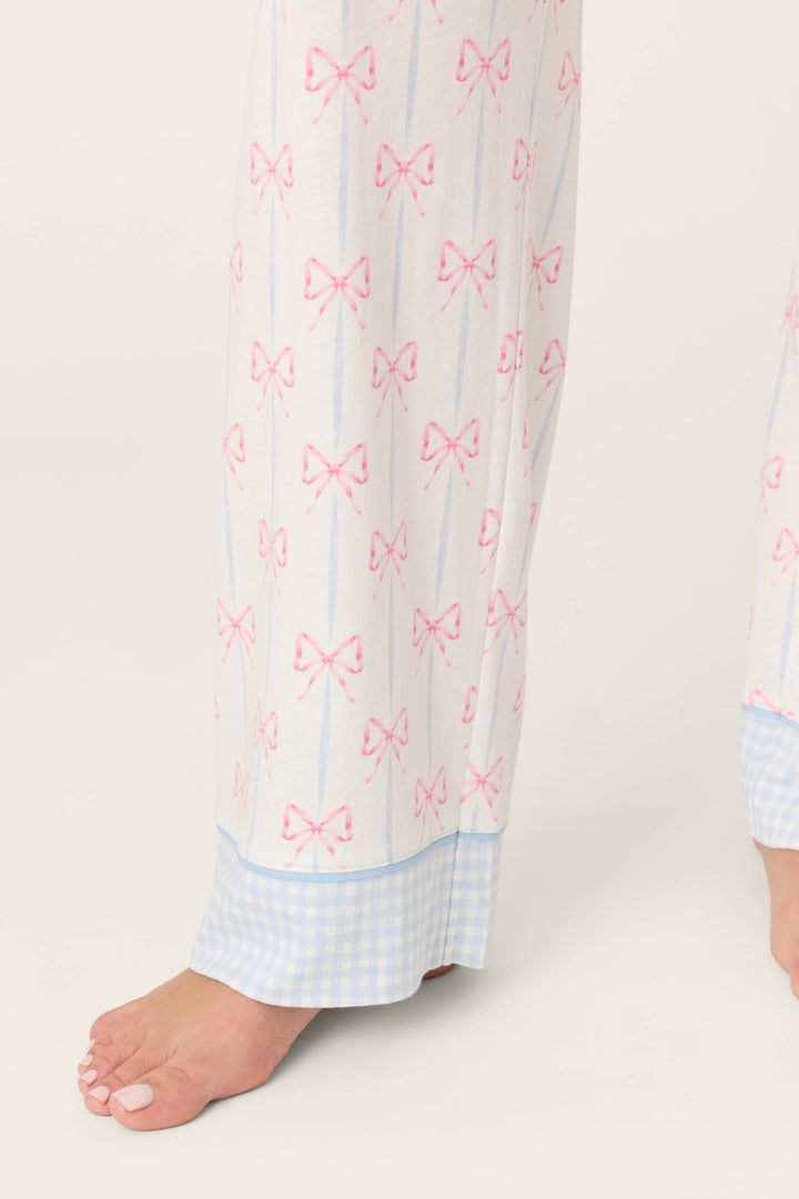 A person models the P.J. Salvage Playful Prints All Wrapped Up Open Leg PJ Pants, featuring bow prints and blue gingham cuffs, standing barefoot on a light background with only their lower legs and feet visible.