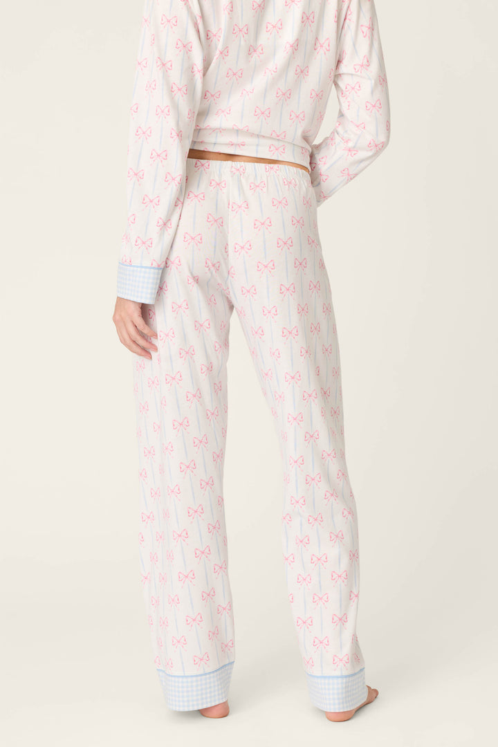 A person stands barefoot facing away, wearing P.J. Salvage’s Playful Prints All Wrapped Up Open Leg PJ Pants with a bow print, drawstring waist, blue checkered cuffs, and open-leg silhouette, set against a plain light beige background.