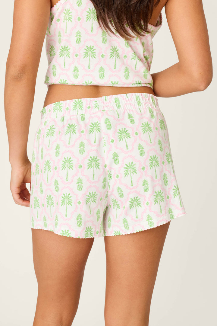 A person is seen from the back wearing P.J. Salvage Playful Prints Island Time PJ Shorts, featuring a tropical pineapple and palm tree print on ivory cotton-modal jersey with an elastic waistband.