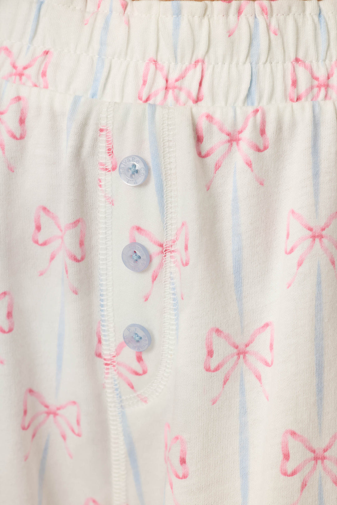 White cotton-modal jersey with light blue stripes, pink bow motif, and three light blue buttons; soft and cozy texture.