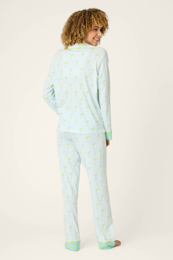 Model stands barefoot, smiling over their shoulder with curly hair, in the P.J. Salvage Playful Prints Salty Cadillac Striped Long PJ Set—featuring a fun pineapple print and green accents in soft cotton-modal jersey—against a plain background.