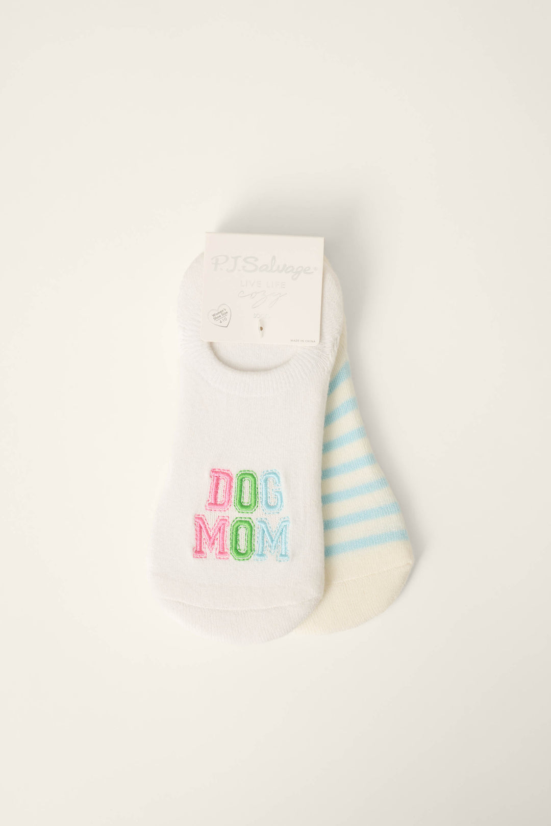 The P.J. Salvage Pupcation Palms Dog Mom 2-Pack Cushion Liner Socks includes one white pair with colorful DOG MOM embroidery and one pair with light blue and white stripes, both shown with a paper label attached at the top.