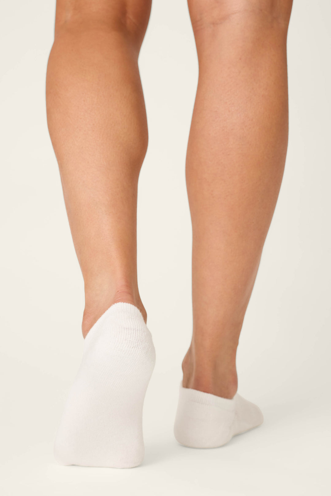 A person stands on a light background, shown from the calves down, wearing P.J. Salvage Pupcation Palms Dog Mom 2-Pack Cushion Liner Socks. The white, low-cut socks have cushioned soles; one heel is slightly raised.