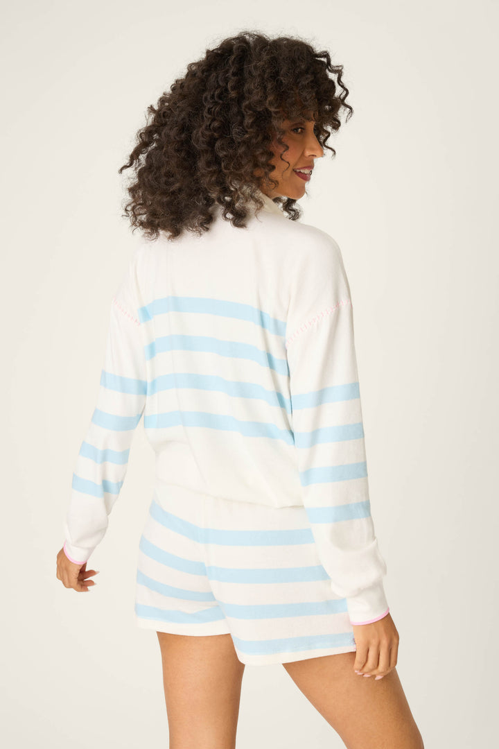 A person with curly hair is shown from the back, wearing the P.J. Salvage Pupcation Palms Ocean Stripe Quarter Zip Pullover Sweater, featuring a relaxed silhouette and light blue stripes, against a plain light background.