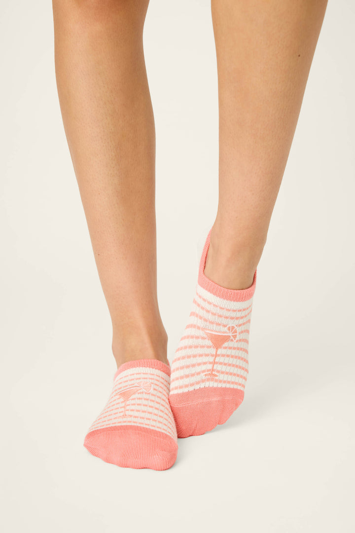 Two feet wear P.J. Salvage Paloma Mama Sweet Sips 2-Pack No Show Sock Liners, featuring pink and white stripes with a martini glass motif, against a plain light background.