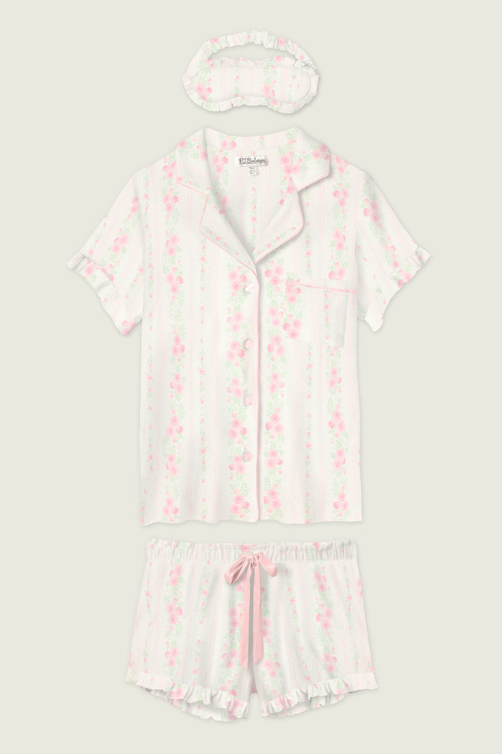 The P.J. Salvage Roses Are Pink Petal Dream Pointelle 3-Piece PJ Set includes a short-sleeved button-up top, matching shorts with a pink ribbon, and a ruffled sleep mask—all in pink and white vertical stripes with a floral motif.