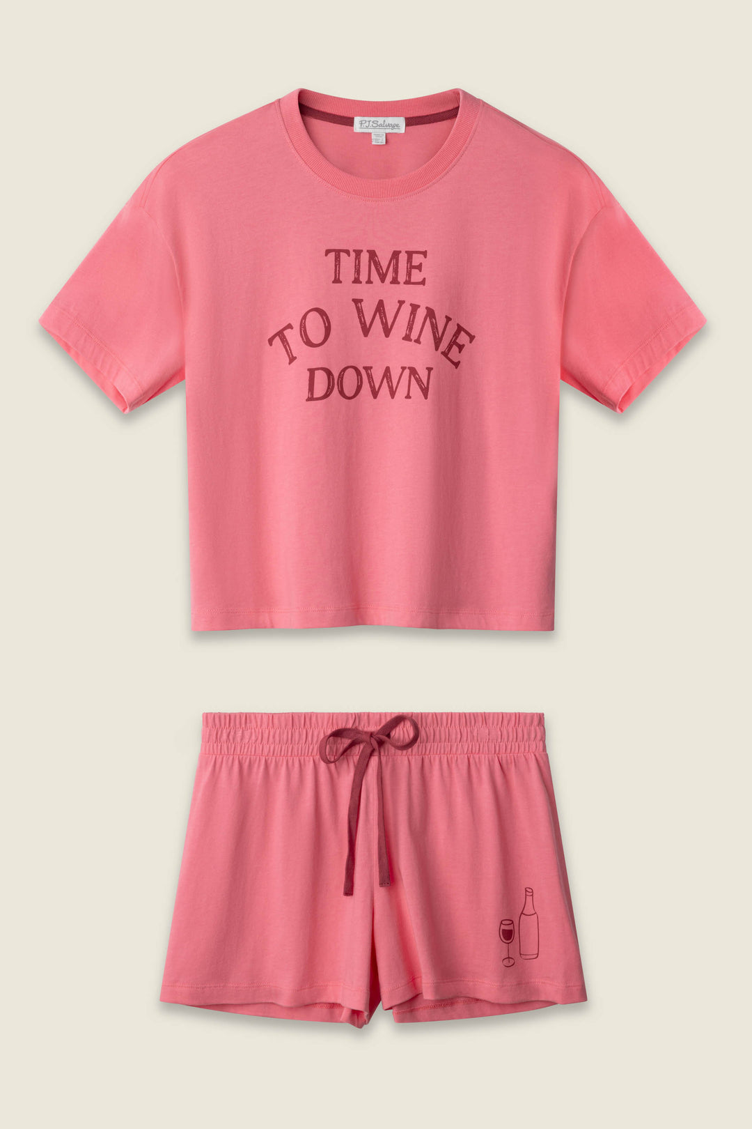 The P.J. Salvage Time to Wine Down Graphic Print Softee Set features a matching pink crop top with “TIME TO WINE DOWN” on the front and drawstring shorts with a wine bottle and glass graphic on one leg.