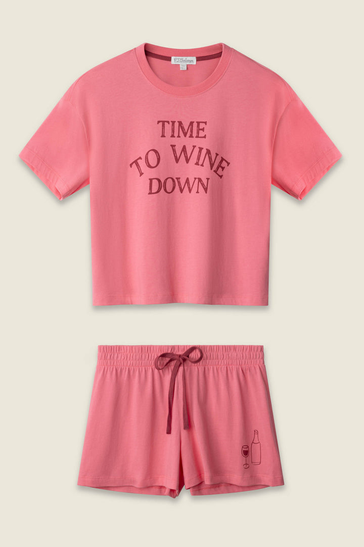 The P.J. Salvage Time to Wine Down Graphic Print Softee Set features a matching pink crop top with “TIME TO WINE DOWN” on the front and drawstring shorts with a wine bottle and glass graphic on one leg.