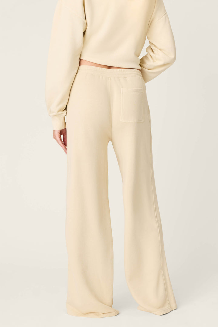 A person stands with their back to the camera, wearing P.J. Salvage Washed Away Lake Life For Life Open Leg Pants in cream French terry, styled with a matching cropped sweatshirt; the pants have a right-side back pocket.
