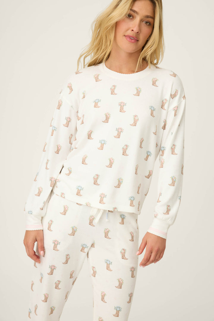 A woman wears the P.J. Salvage Western Blooms Boot Bouquet Long Sleeve Top, a white pajama set with a repeated small otter print, standing slightly turned against a plain light background.