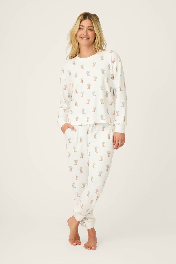 A woman stands barefoot against a plain background, wearing the P.J. Salvage Western Blooms Boot Bouquet Long Sleeve Top. She has her left hand in her pocket and smiles at the camera.