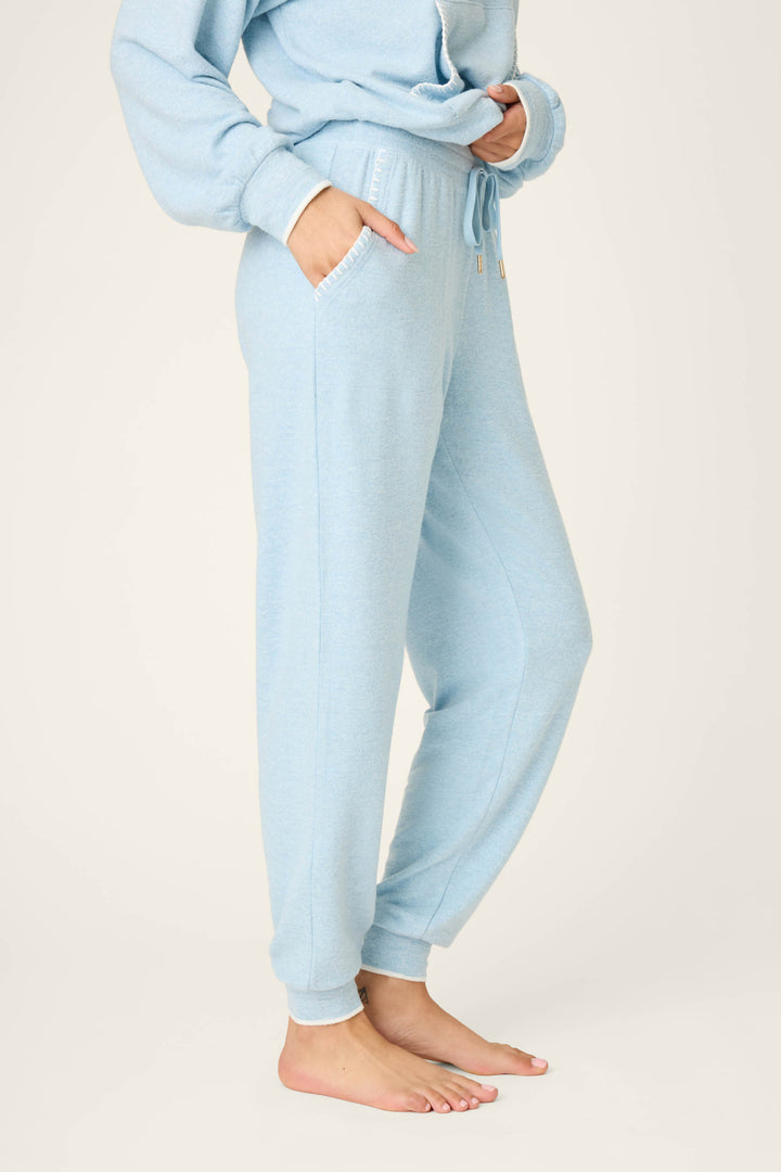 A person stands barefoot with hands in pockets, showing only the lower half of their body while wearing P.J. Salvage’s Western Blooms Dream Blue Banded Pants against a plain background.