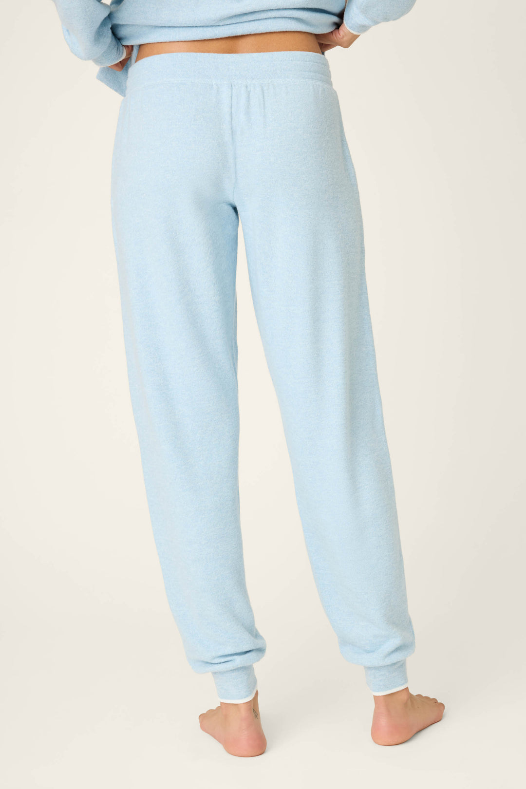 A person stands barefoot on a light surface wearing P.J. Salvage's Western Blooms Dream Blue Banded Pants, shown in a back view from the waist down with light blue fabric and cuffed hems.