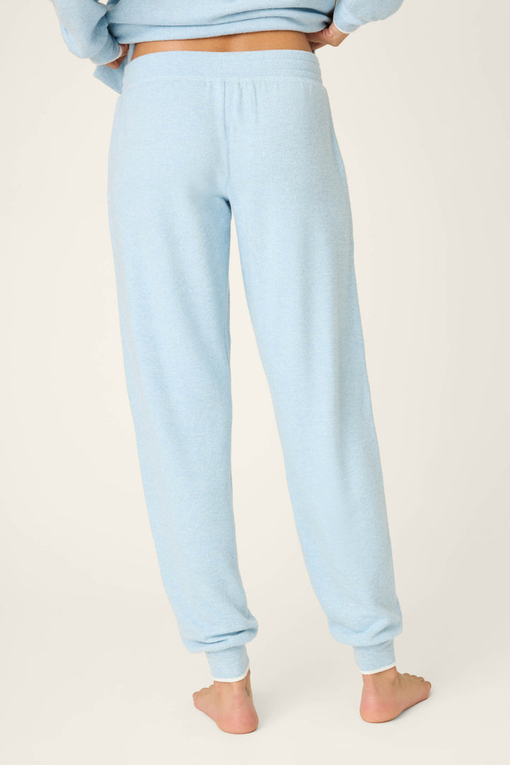 A person stands barefoot on a light surface wearing P.J. Salvage's Western Blooms Dream Blue Banded Pants, shown in a back view from the waist down with light blue fabric and cuffed hems.