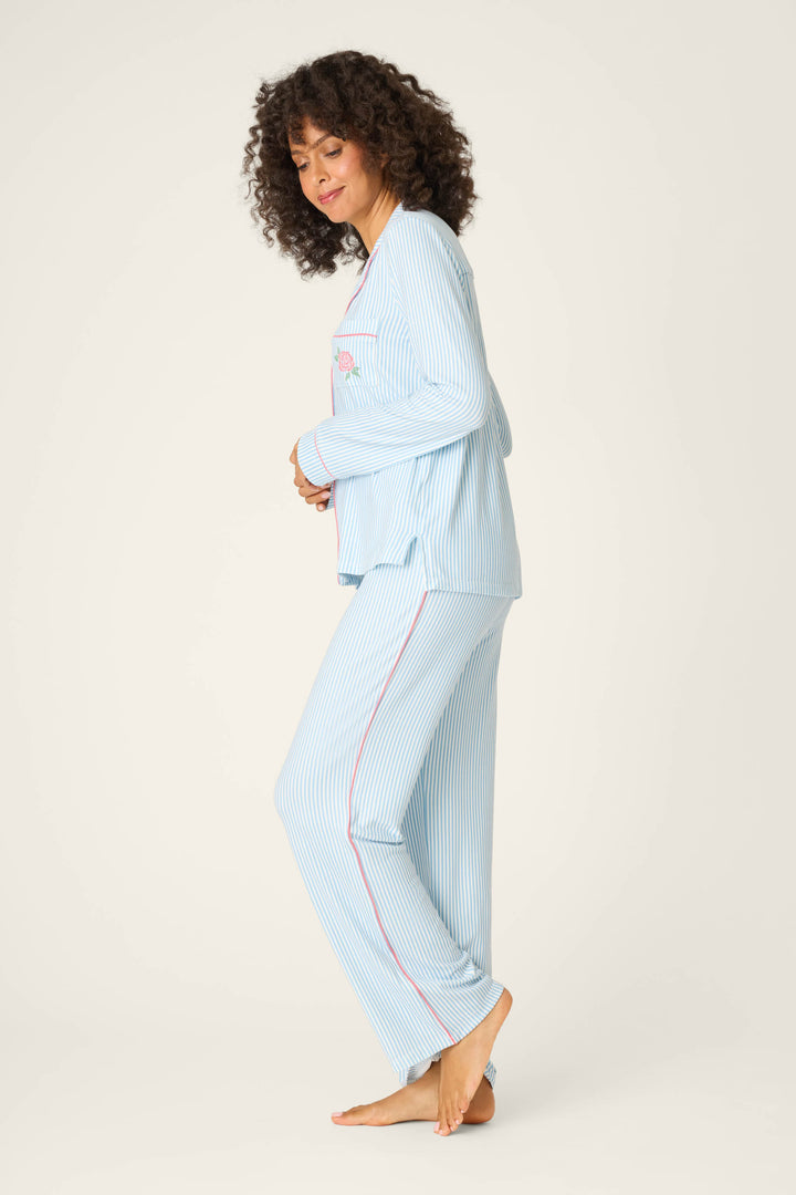 A person with curly hair stands barefoot on one leg, wearing the P.J. Salvage Western Blooms Blue Stripe Darlin 3-Piece PJ Set, against a plain off-white background.
