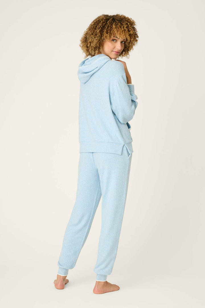 A person with curly hair stands barefoot on a light background, wearing the P.J. Salvage Western Blooms Dream Blue Lounge Set, looking over their shoulder and smiling slightly.