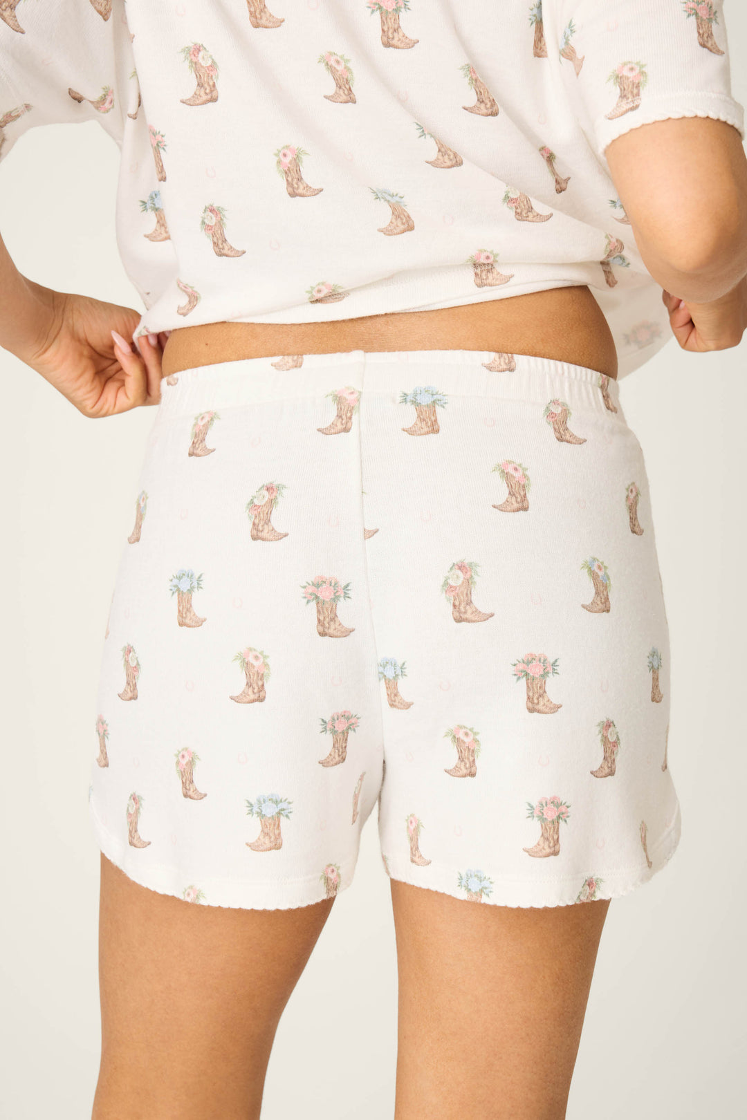 Model wears P.J. Salvage Western Blooms Boot Bouquet Shorts—white pajama shorts with a blue flower and cowboy boot print—shown from the waist down against a plain background.
