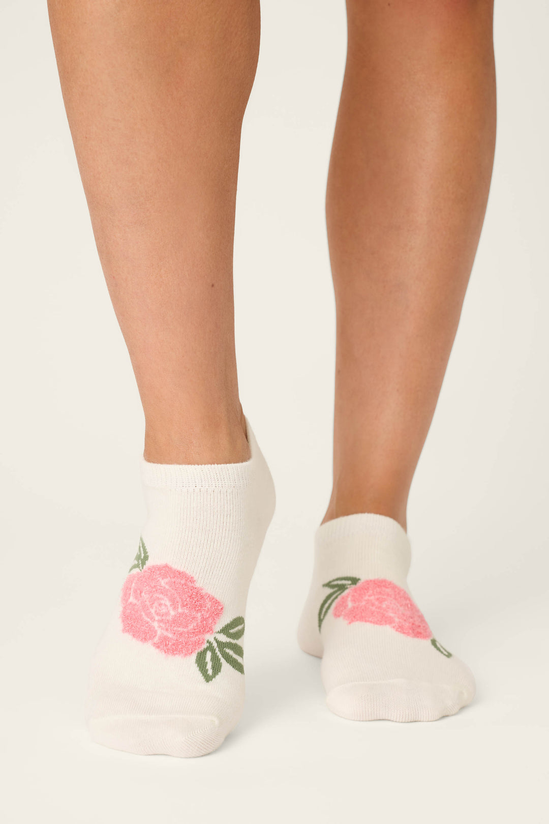 A person wearing P.J. Salvage Western Blooms Rose Stripe 3-Pack Ankle Socks featuring pink rose and green leaf designs stands on a light-colored surface.