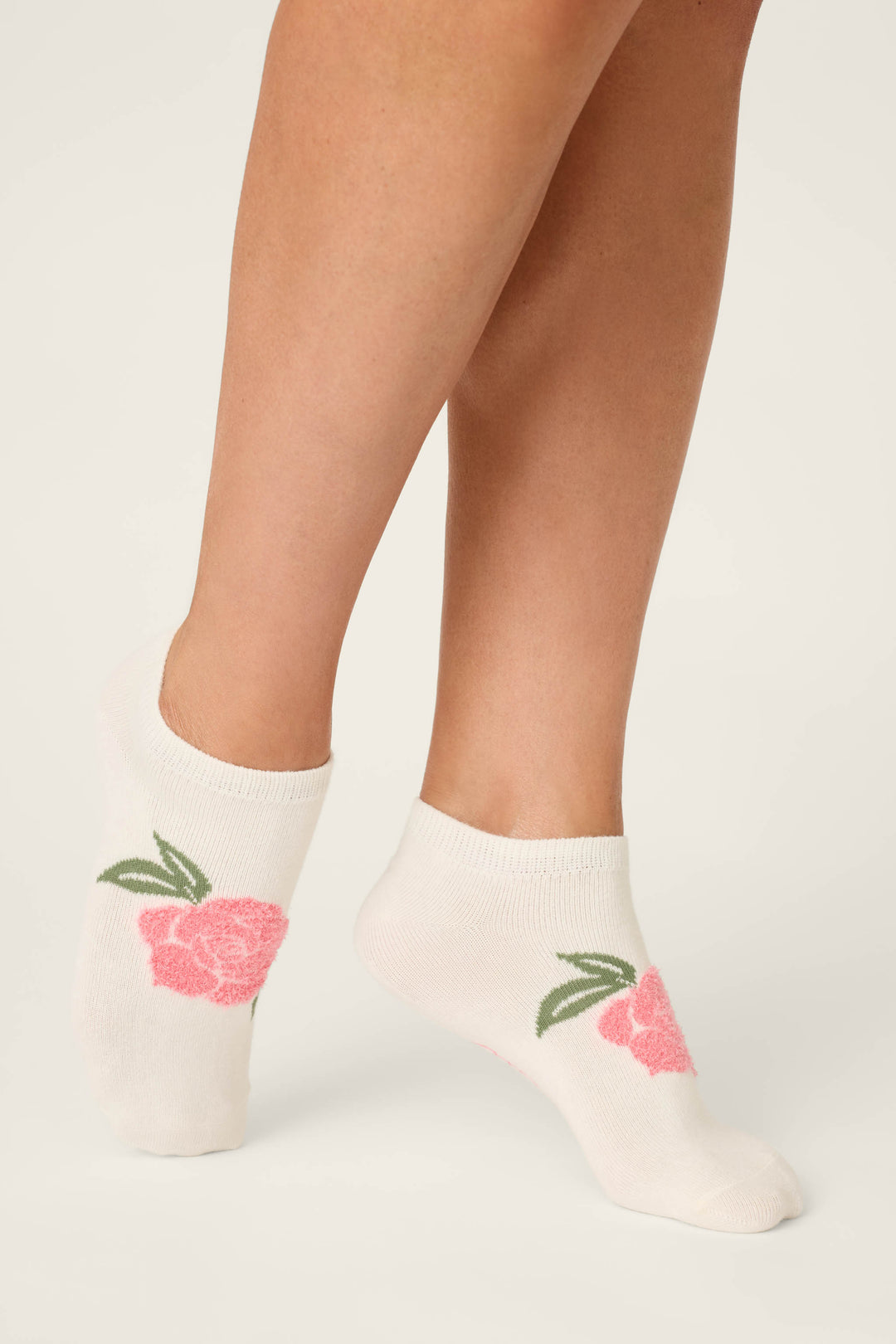 A person wearing P.J. Salvage Western Blooms Rose Stripe 3-Pack Ankle Socks with pink flower and green leaf designs stands on tiptoe against a plain light background.