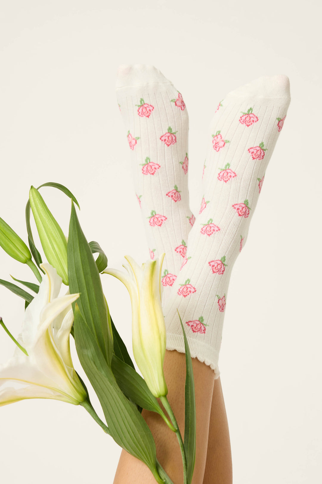 Someone wearing P.J. Salvage Western Blooms Roses Ribbed Crew Socks holds their legs up next to a bouquet of white lilies against a simple light backdrop.