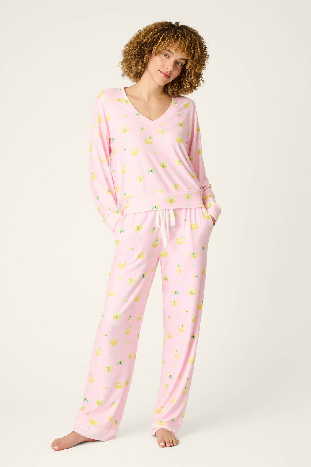 A person stands barefoot against a plain light background, wearing a matching pink pajama set with a V-neck and long sleeves.