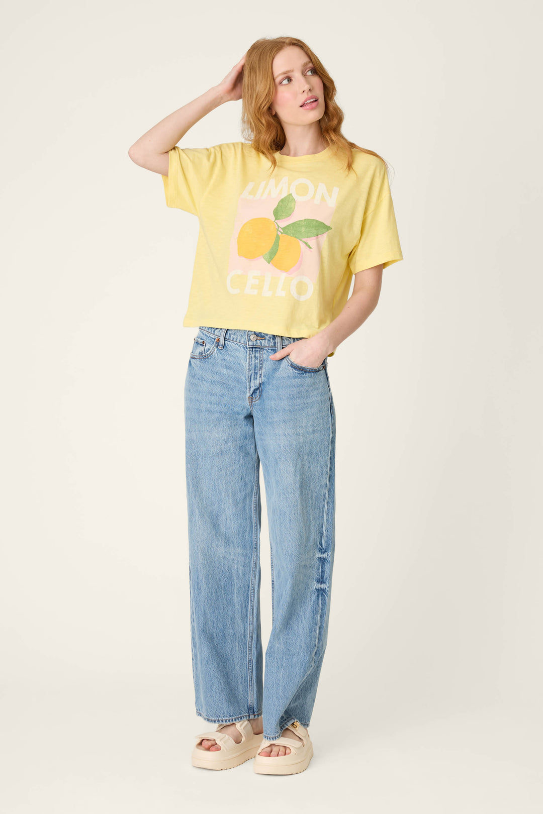 Against a plain background, a person wears a yellow graphic tee with light blue high-waisted jeans and beige platform sandals.