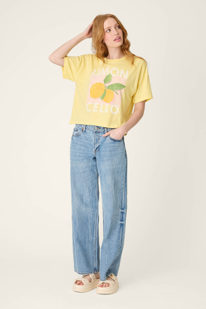 Against a plain background, a person wears a yellow graphic tee with light blue high-waisted jeans and beige platform sandals.