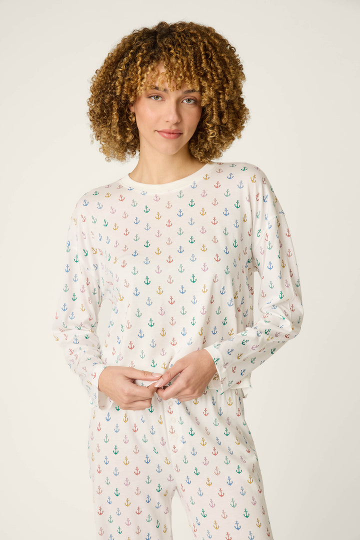 A person with curly hair is wearing the P.J. Salvage Meet Me By The Sea Anchor Rainbow Long Sleeve Top, standing against a plain light background.